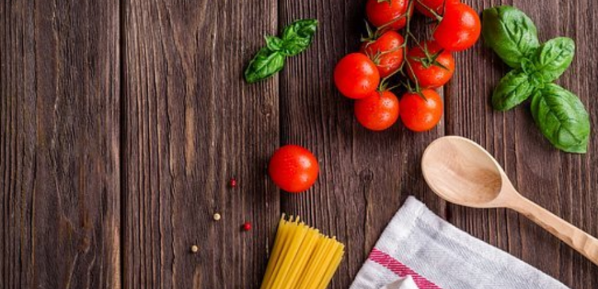 Et billede af spaghetti, røde tomater og grøn basilikum på en brun bordplade